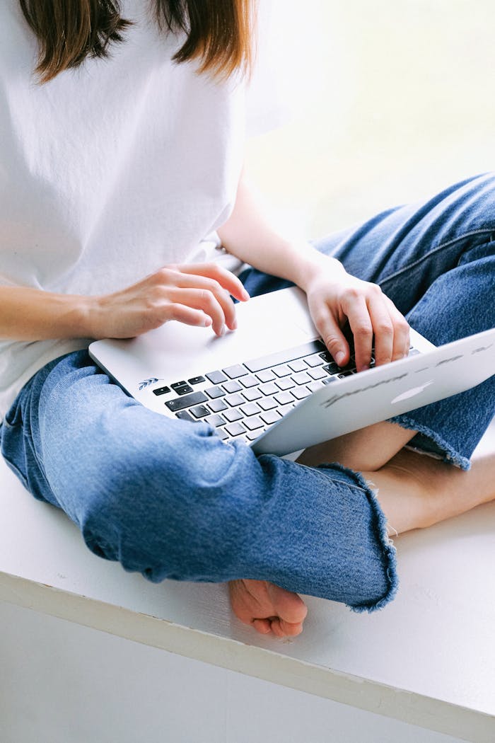 Woman sitting cross-legged in casual jeans working on a laptop indoors.